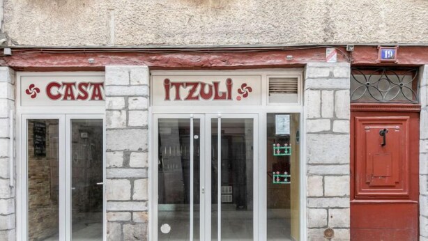 A building facade with a stone exterior, two glass doors with the signs "CASA" and "ITZULI" above them, and a red door to the right. - Casa Itzuli by Interhome (Bayonne)