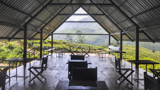 A covered outdoor seating area with tables and chairs, overlooking a lush valley. - Wild Glamping (Rangala)