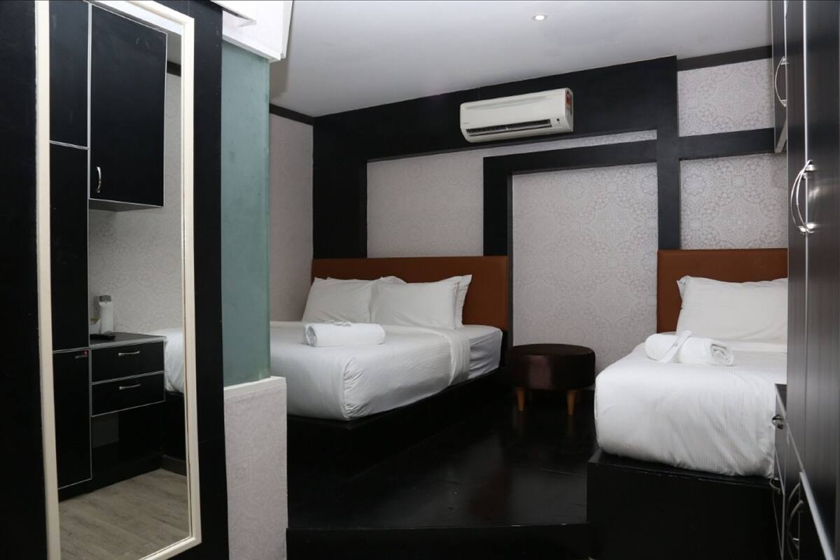 Ein Hotelzimmer mit zwei Betten, einem kleinen Tisch, einem Kleiderschrank und einer Klimaanlage.