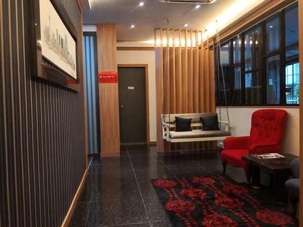 Un hall d’entrée moderne avec un sol carrelé de noir, un fauteuil rouge, une balançoire en bois et un tableau représentant un paysage urbain.