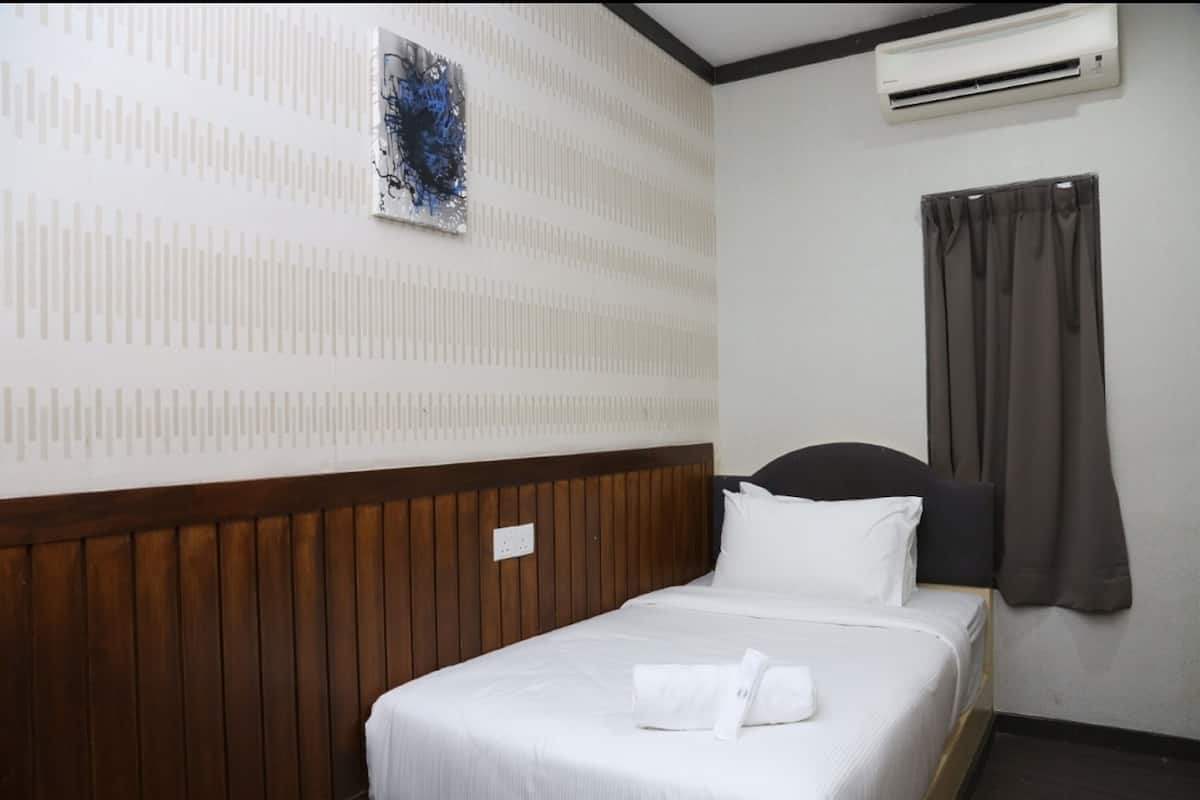 Ein Hotelzimmer mit einem hölzernen Kopfteil, einem Bett mit weißer Bettwäsche, einer Wand-Klimaanlage und einem Fenster mit Vorhängen.
