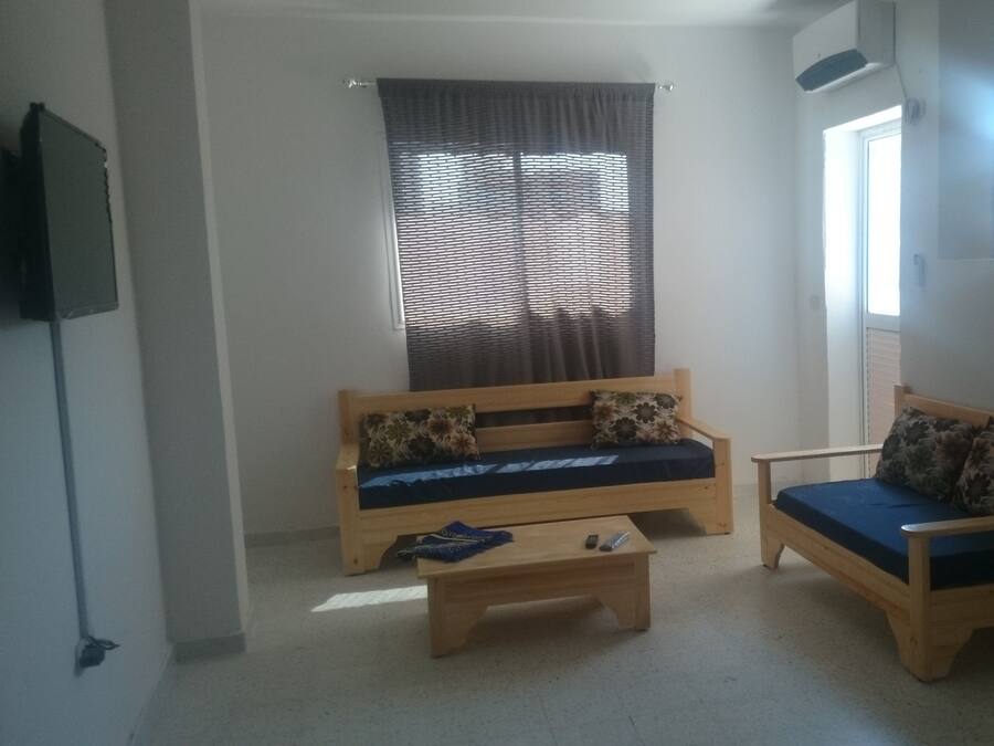 Una sala de estar pequeña y acogedora con dos sofás de madera, una mesita de centro y un televisor montado en la pared.