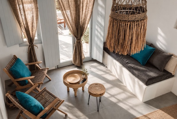 A room with a sofa, two wicker chairs, a small round table, and a woven hanging chair.