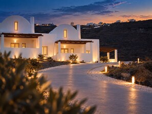 A modern villa with a curved driveway, white exterior, and multiple windows. - Bianco Diverso Suites (Santorini)