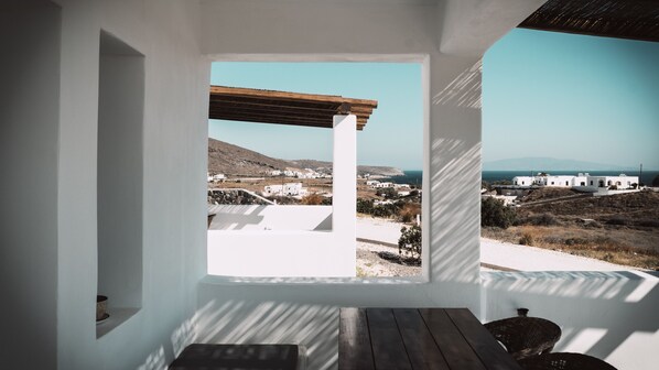 Quarto com vista para a paisagem costeira, uma mesa de madeira e uma parede branca.