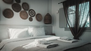 A neatly made bed with white linens, a headboard, and a window with curtains. - Bianco Diverso Suites (Santorini)