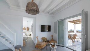 A modern interior with a staircase, a flat-screen TV, wicker furniture, and a view to the outside. - Bianco Diverso Suites (Santorini)