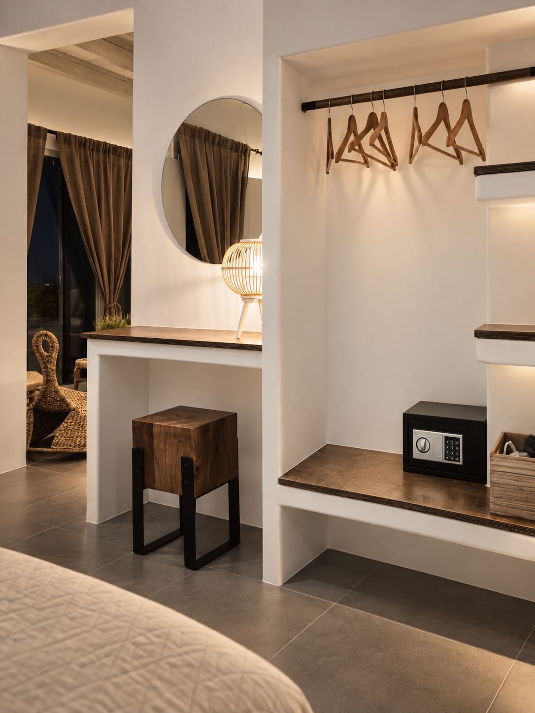 A modern bedroom with a bed, a bedside table, a small wooden stool, a round mirror, a wall-mounted light, and a coat rack.