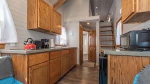 A compact kitchen with wooden cabinets, a coffee maker, a kettle, and a microwave.