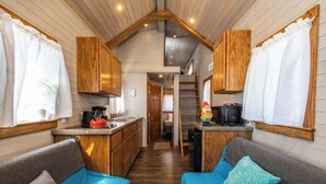 A compact RV interior with a kitchenette, two blue sofas, wooden cabinets, and a small dining area.