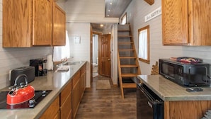 A kitchen with wooden cabinets, a red kettle, a microwave, and a ladder leading to a loft.
