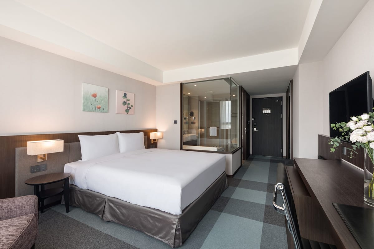 A hotel room with a large bed, bedside tables with lamps, a desk with a vase of flowers, and a mirror.