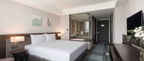 A hotel room with a large bed, bedside tables with lamps, a desk with a vase of flowers, and a mirror.