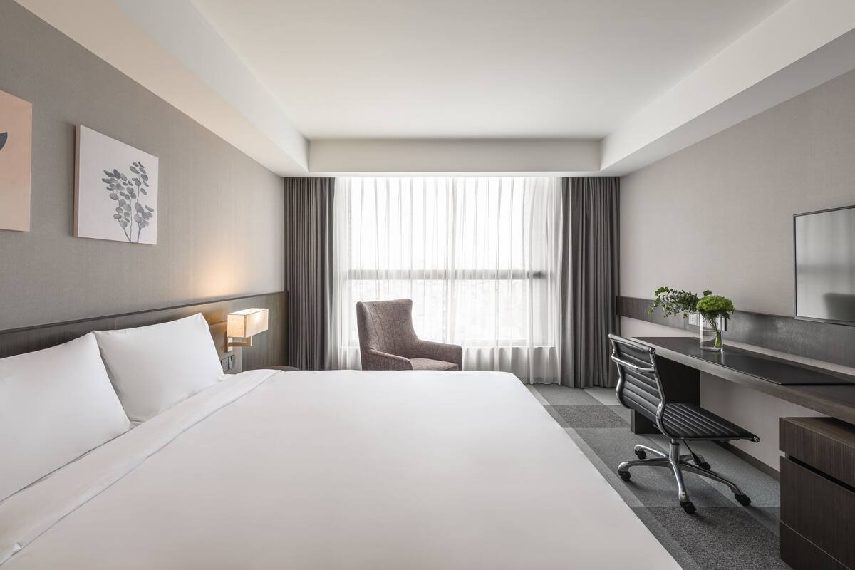 A hotel room with a large bed, a desk with a chair, a TV, and a window with curtains.