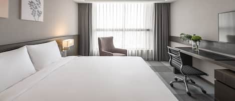A hotel room with a large bed, a desk with a chair, a TV, and a window with curtains.