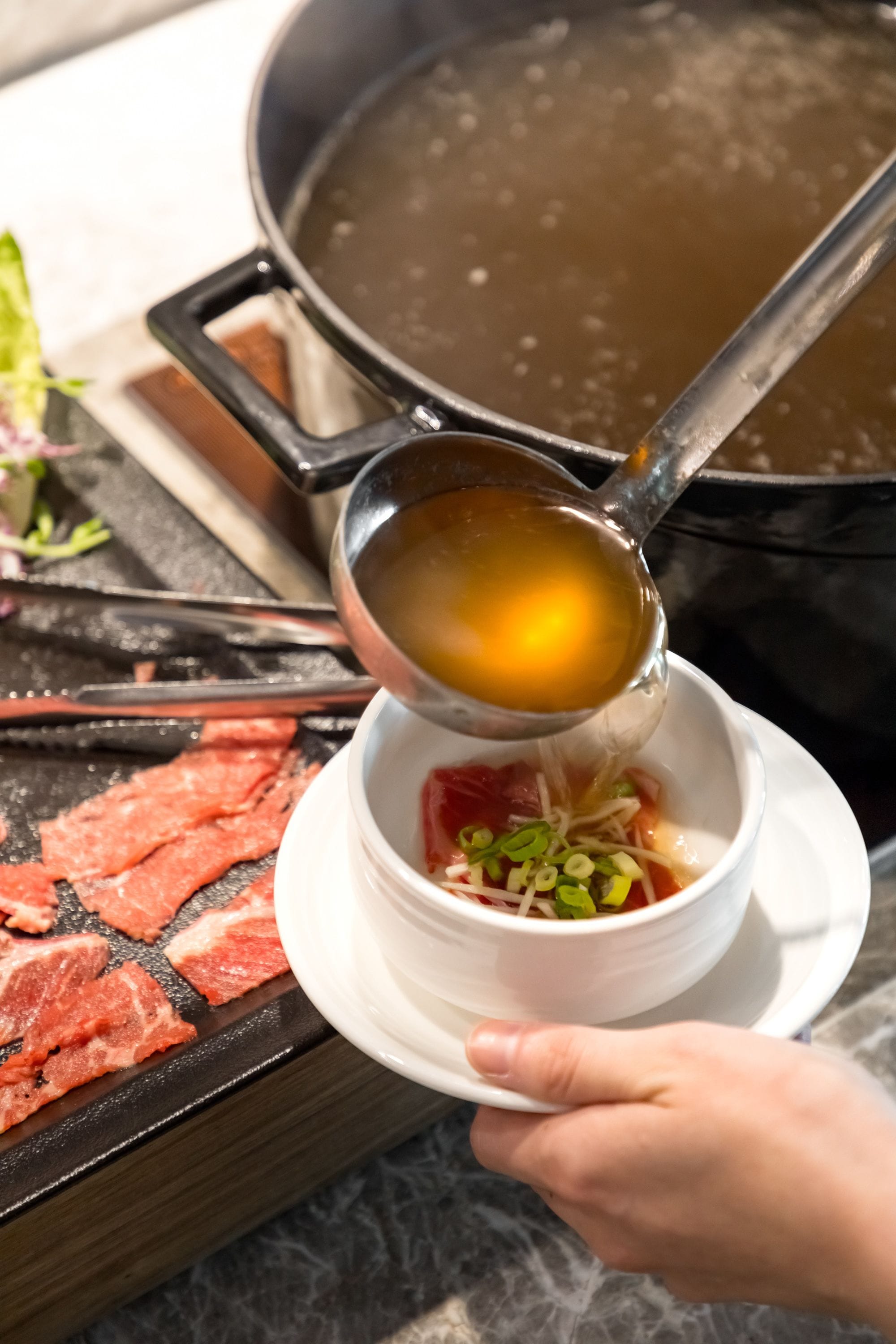 A person pouring a clear liquid into a bowl containing raw meat and vegetables.