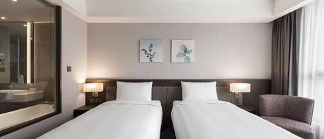 A hotel room with two single beds, a large mirror, a bathroom with a sink and mirror, and two wall-mounted lamps.