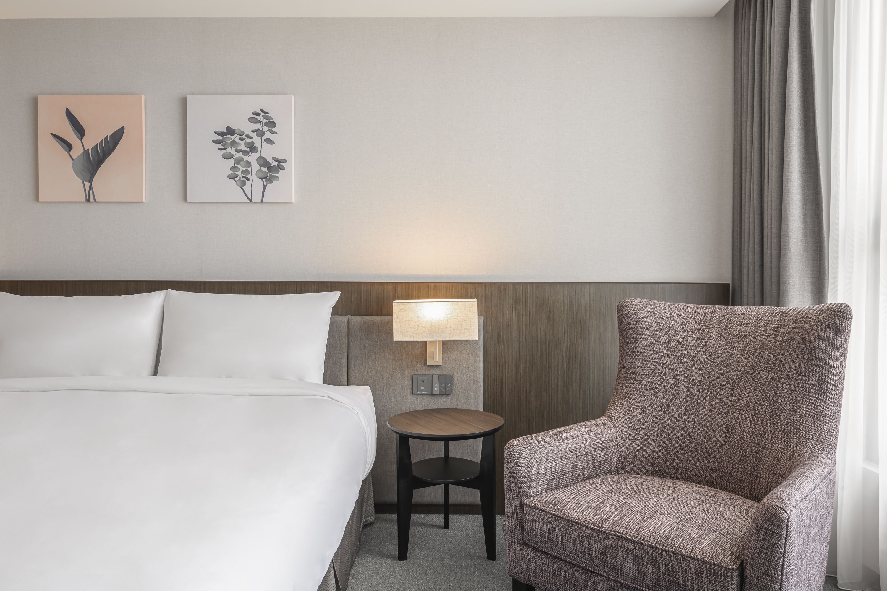 Een hotelkamer met een bed, een stoel, een tafeltje en twee wandlampen.