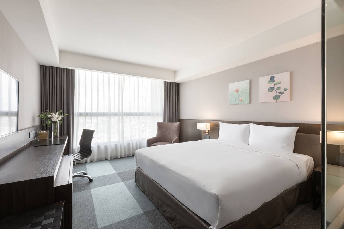 A hotel room with a large bed, a desk with a chair, a TV, and a window with curtains.