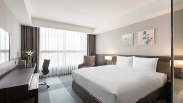 A hotel room with a large bed, a desk with a chair, a TV, and a window with curtains.
