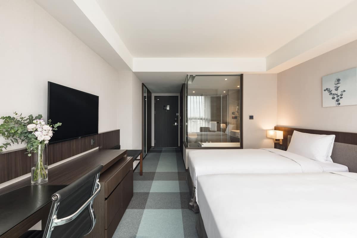 A hotel room with a bed, a desk, a chair, a television, and a vase with flowers.