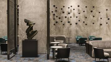 A modern lobby with a marble wall, a sculpture, and seating areas.