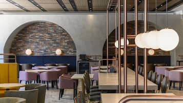 A modern restaurant interior with round tables, purple chairs, and a brick wall.