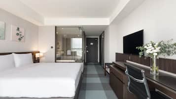 Una habitación de hotel con una cama grande, un escritorio, una silla, un televisor y un florero con flores.