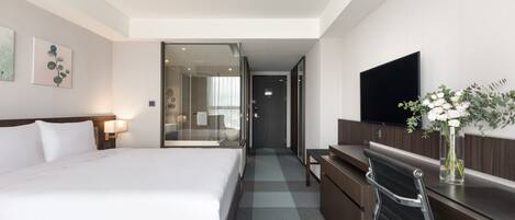 A hotel room with a large bed, a desk, a chair, a TV, and a vase with flowers.