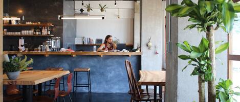 A cafe interior with a bar counter, seating area, and a large potted plant.