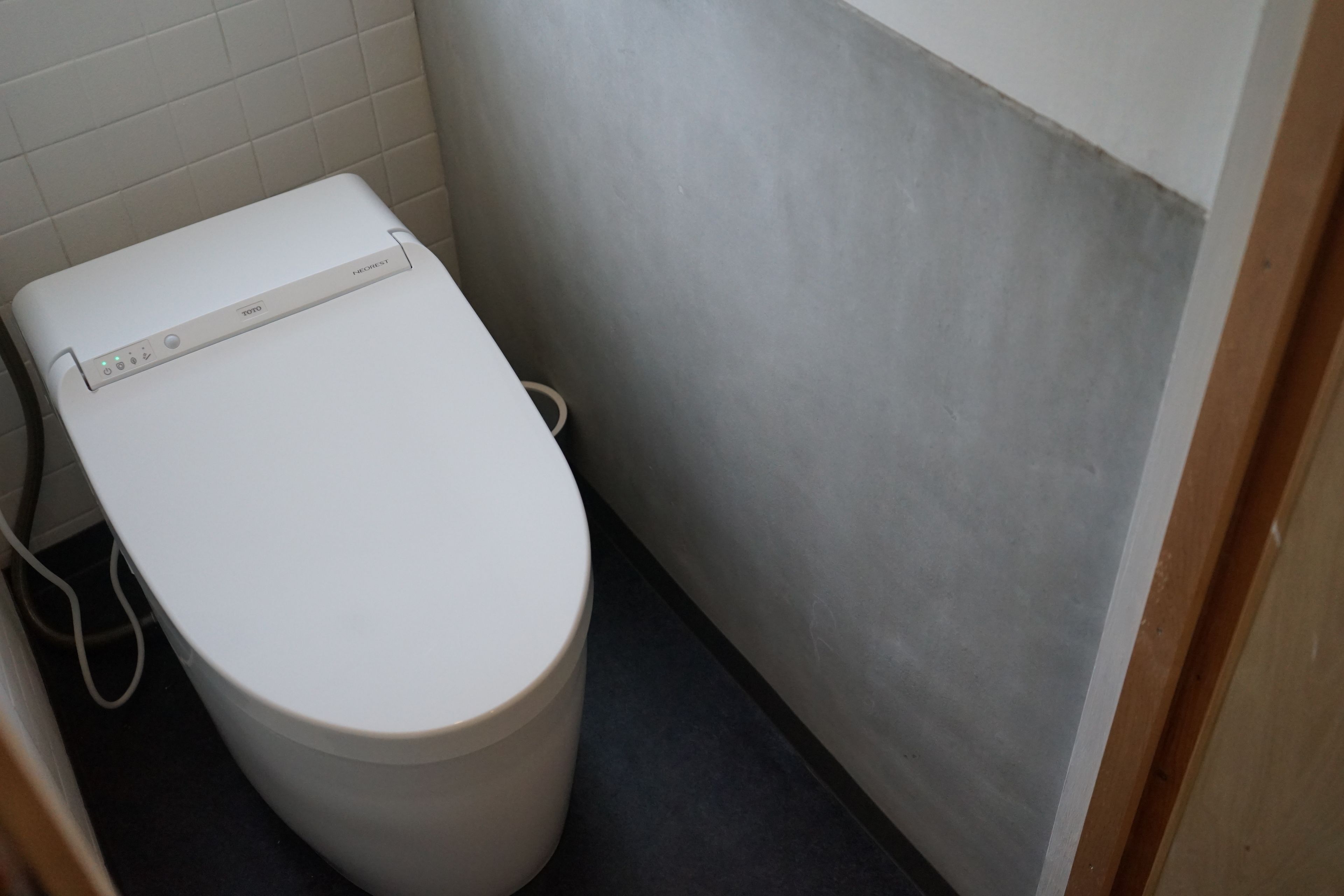 A white toilet with a control panel in a small bathroom with tiled walls and a dark floor.