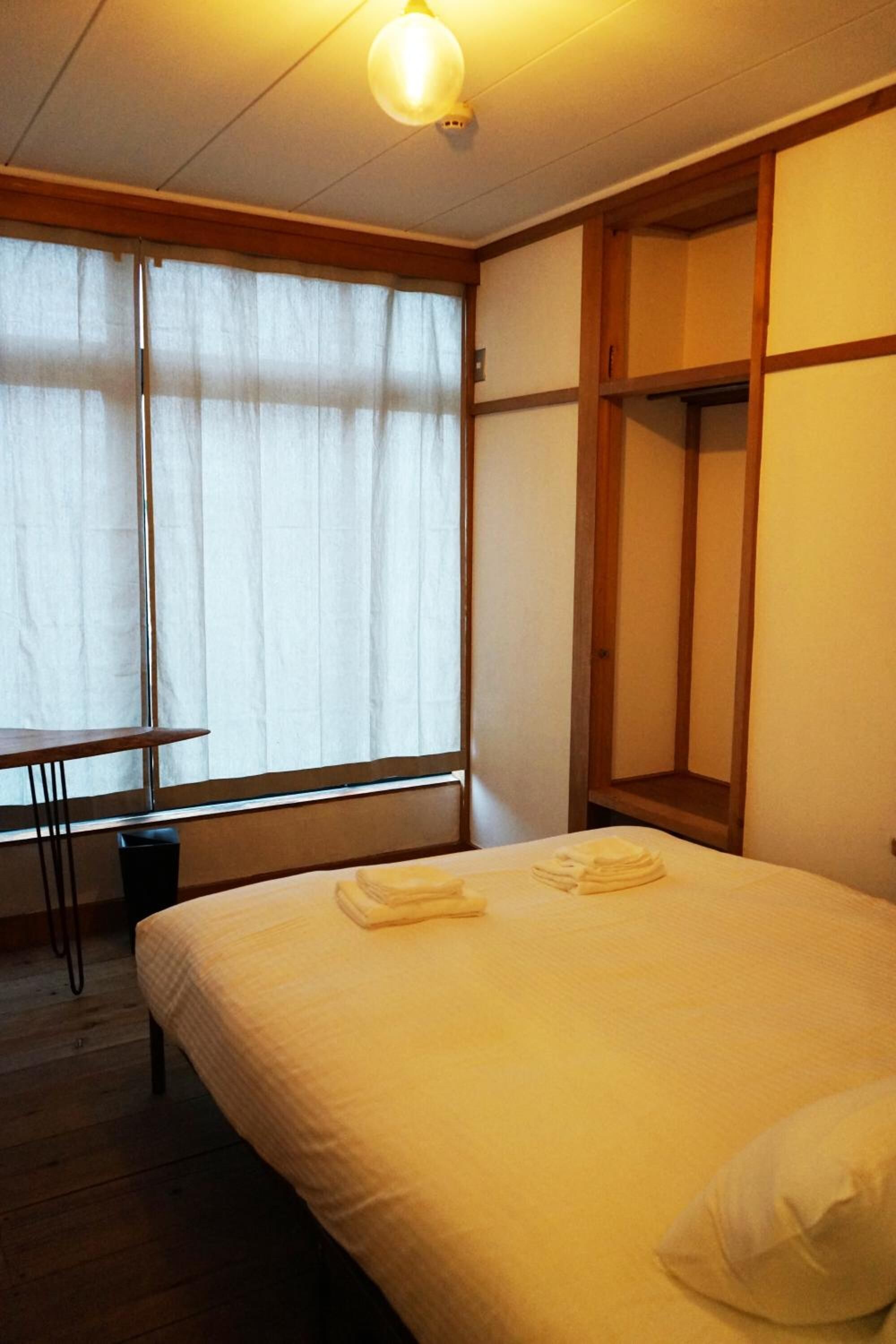 Una habitación de hotel con una cama, una mesita y un ventanal con cortinas.
