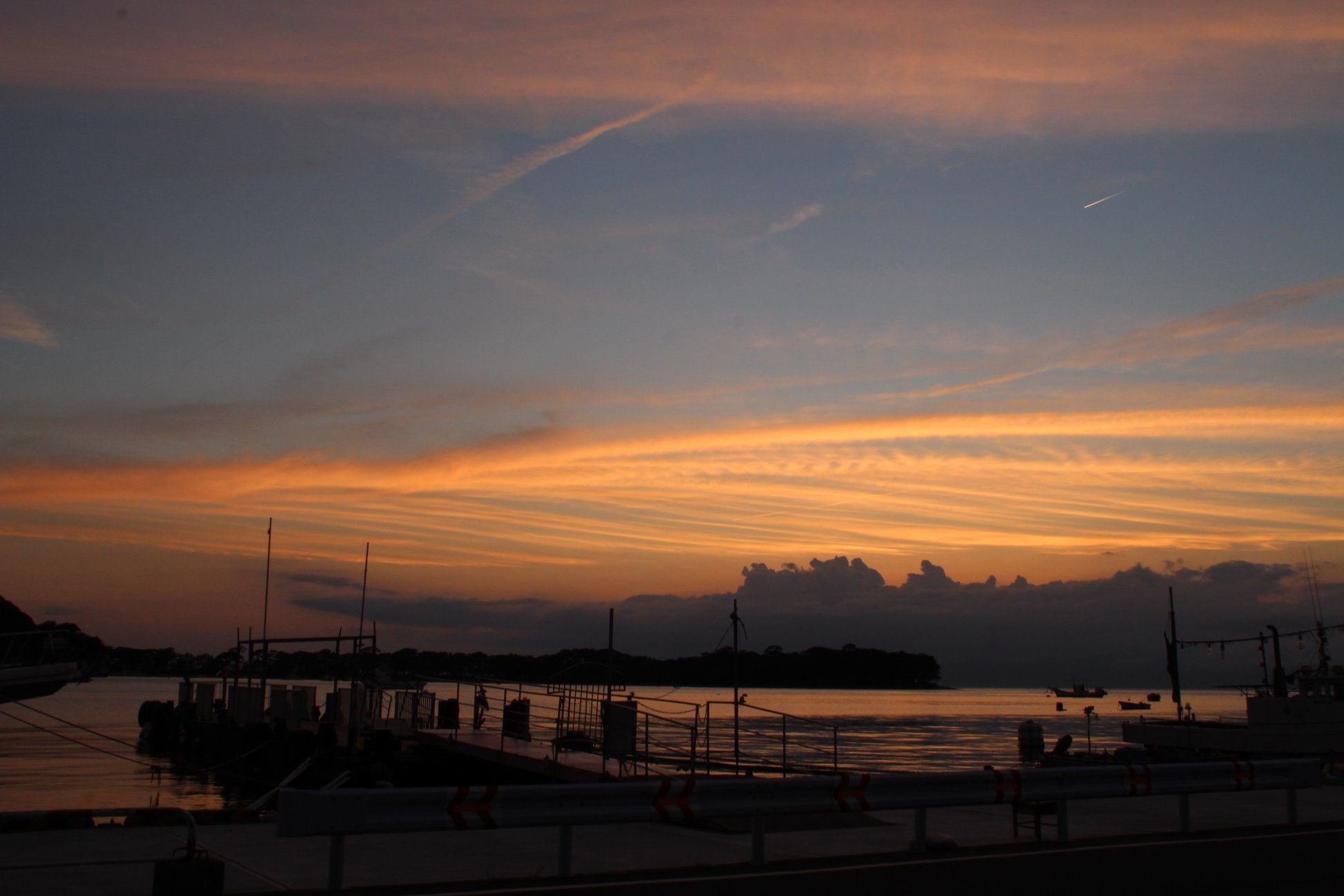 Una vista del atardecer sobre un muelle con barcos amarrados y un espigón que se adentra en el agua.