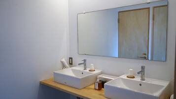 Un baño con dos lavamanos blancos, una encimera de madera y un espejo grande sobre los lavamanos.