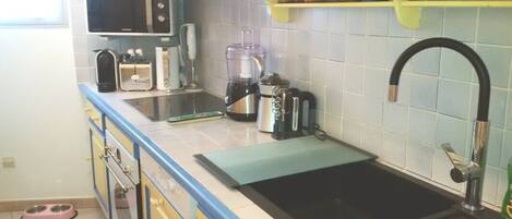 Una cocina equipada con microondas, cafetera, licuadora y un lavamanos con grifo.