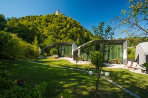 Un jardín tranquilo con una construcción pequeña, un pabellón y un castillo lejano en una colina.