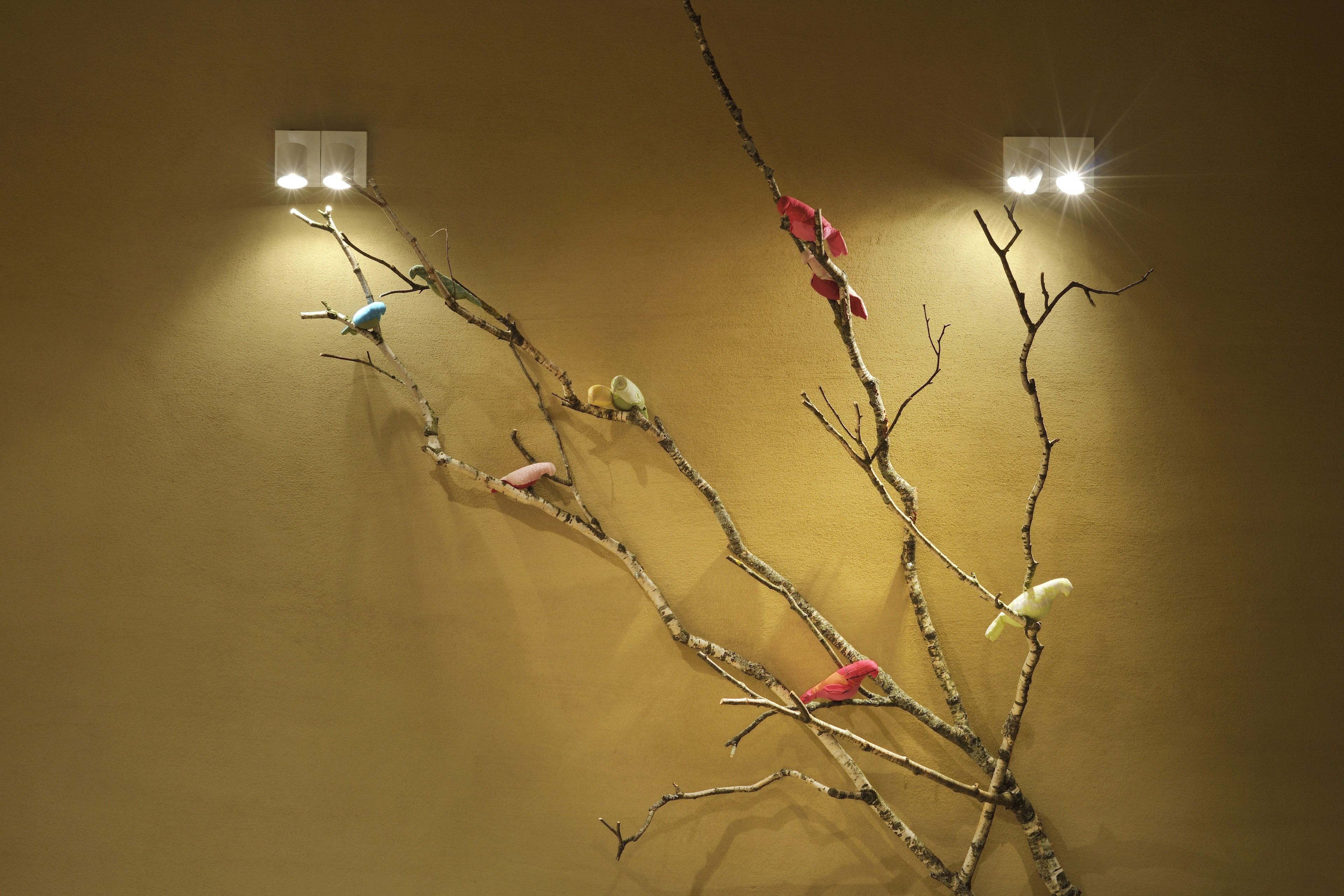 Un mur orné de branches et de petits oiseaux, deux appliques murales et une surface murale texturée.