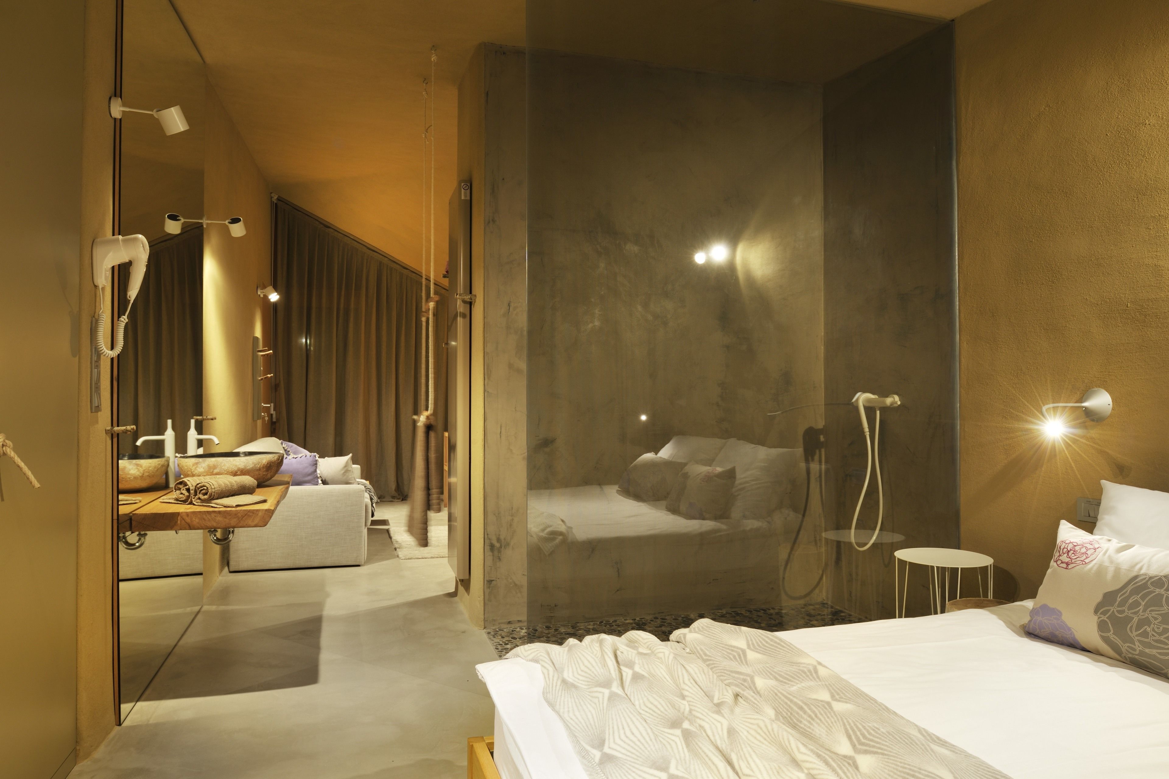 Una habitación de hotel moderna con una cama grande, zona de ducha y tocador con espejo.