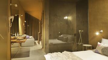 Una habitación de hotel moderna con una cama grande, zona de ducha y tocador con espejo.