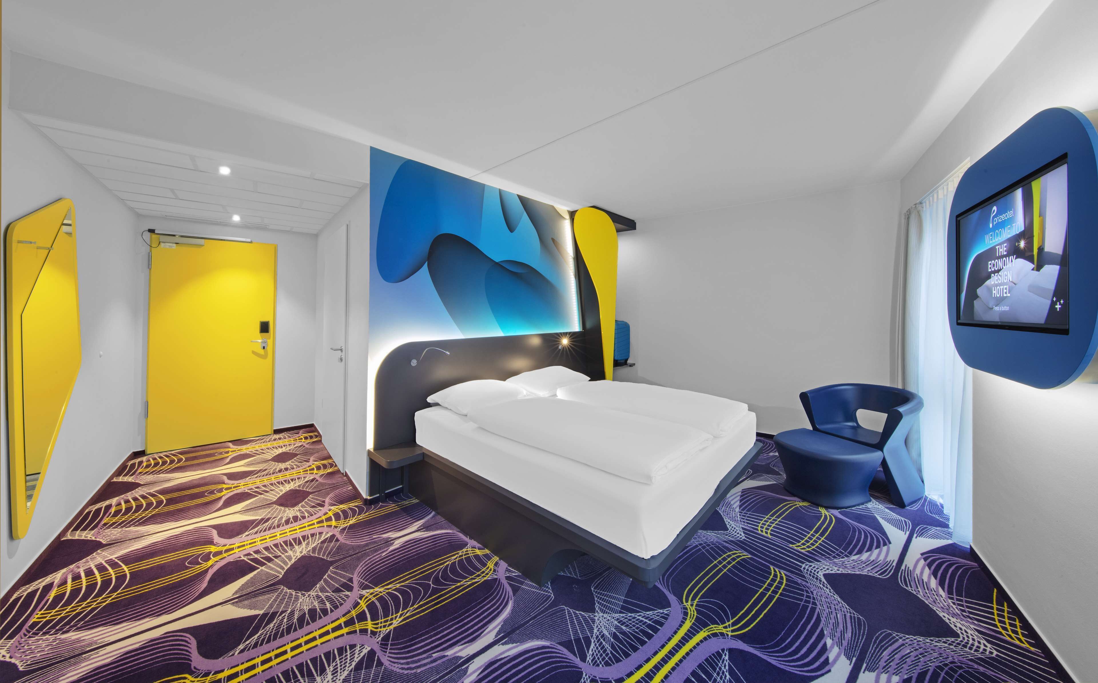Una habitación de hotel moderna con una cama grande, una alfombra de diseño original y un televisor de pared que muestra un mensaje de bienvenida.