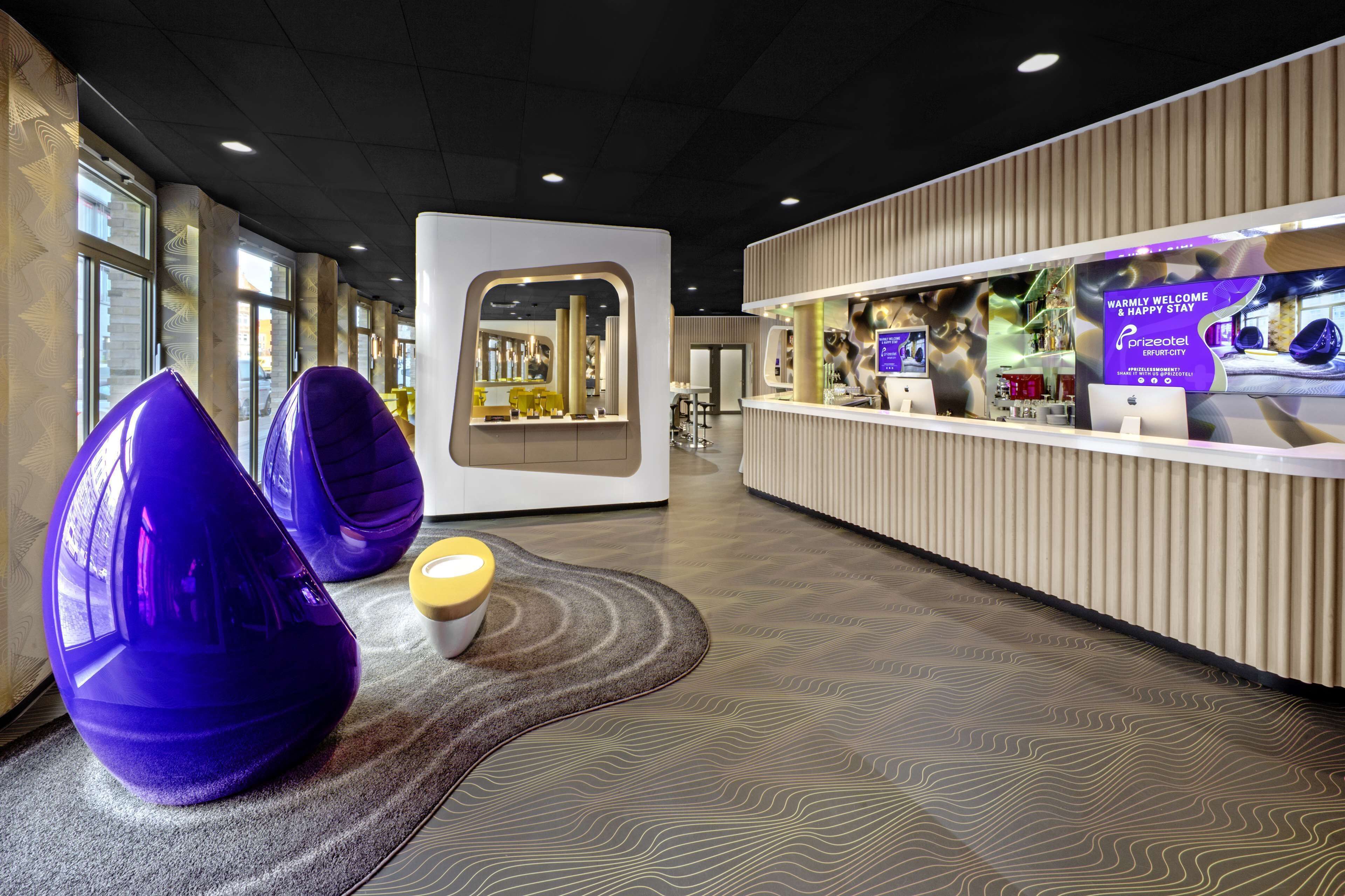 A modern hotel lobby with unique seating, a reception area, and a view of the outside.