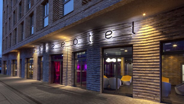 Fachada moderna de hotel con un llamativo letrero que dice 'hotel', amplias ventanas y mobiliario contemporáneo en el interior.