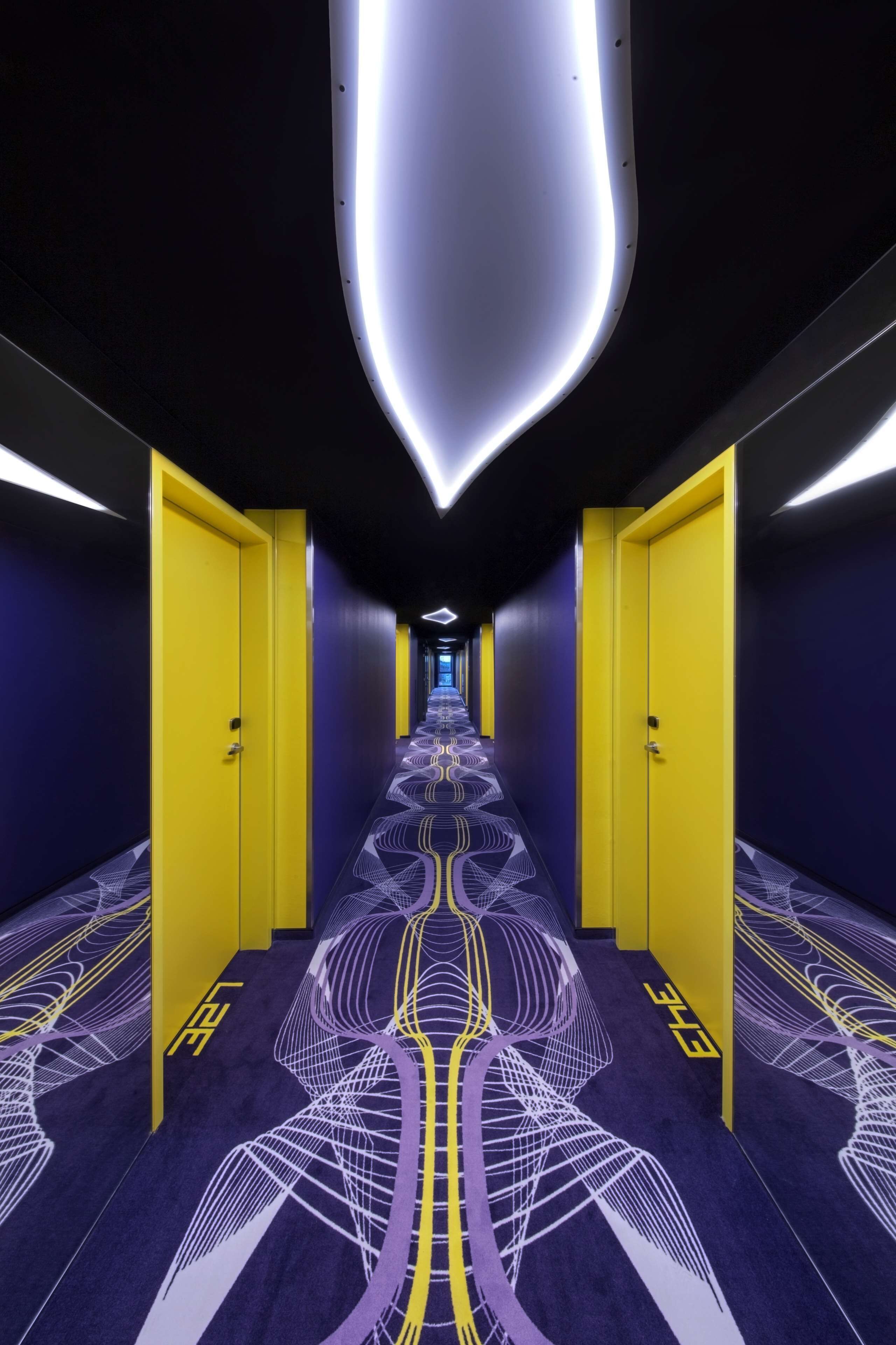 Un couloir avec des portes jaunes, une moquette à motifs et un luminaire moderne.