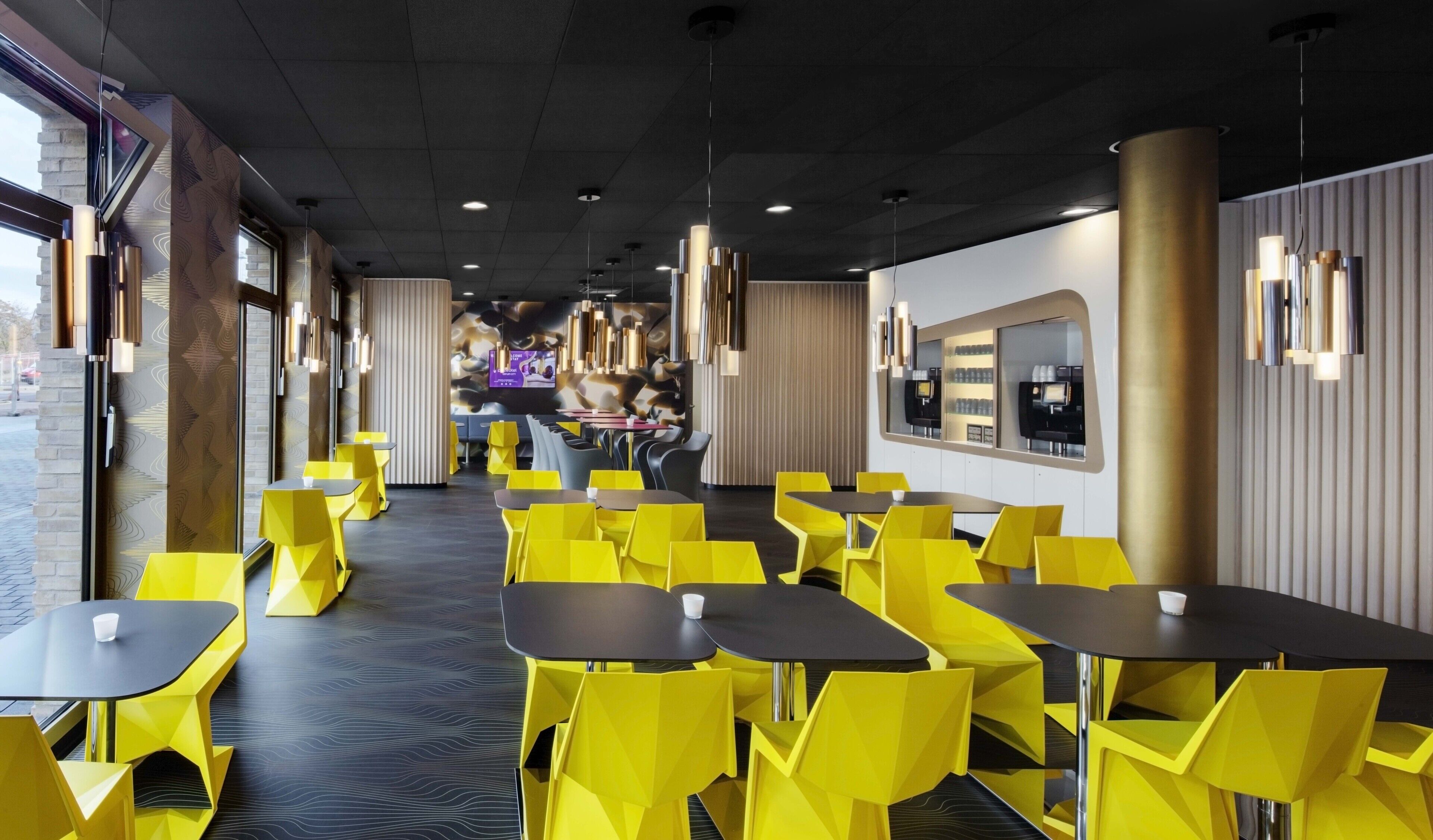 Un interior de restaurante moderno con sillas y mesas amarillas, una barra larga y una pantalla digital con el menú.