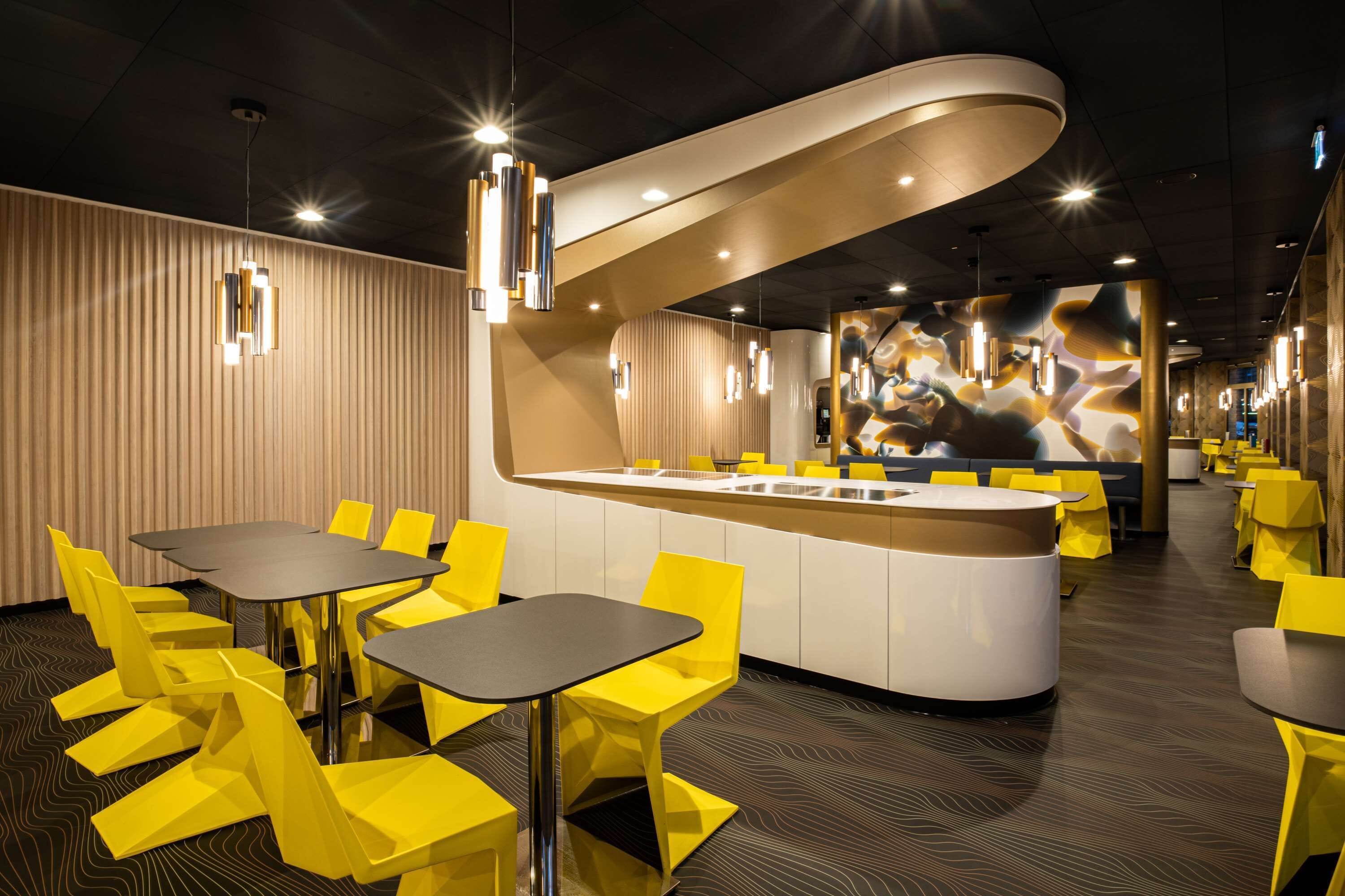 A modern restaurant with yellow chairs and tables, a central island counter, and contemporary lighting fixtures.
