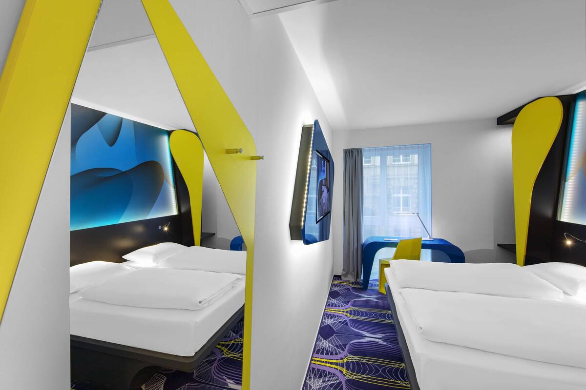 A modern hotel room with two beds, a large mirror, and a TV.