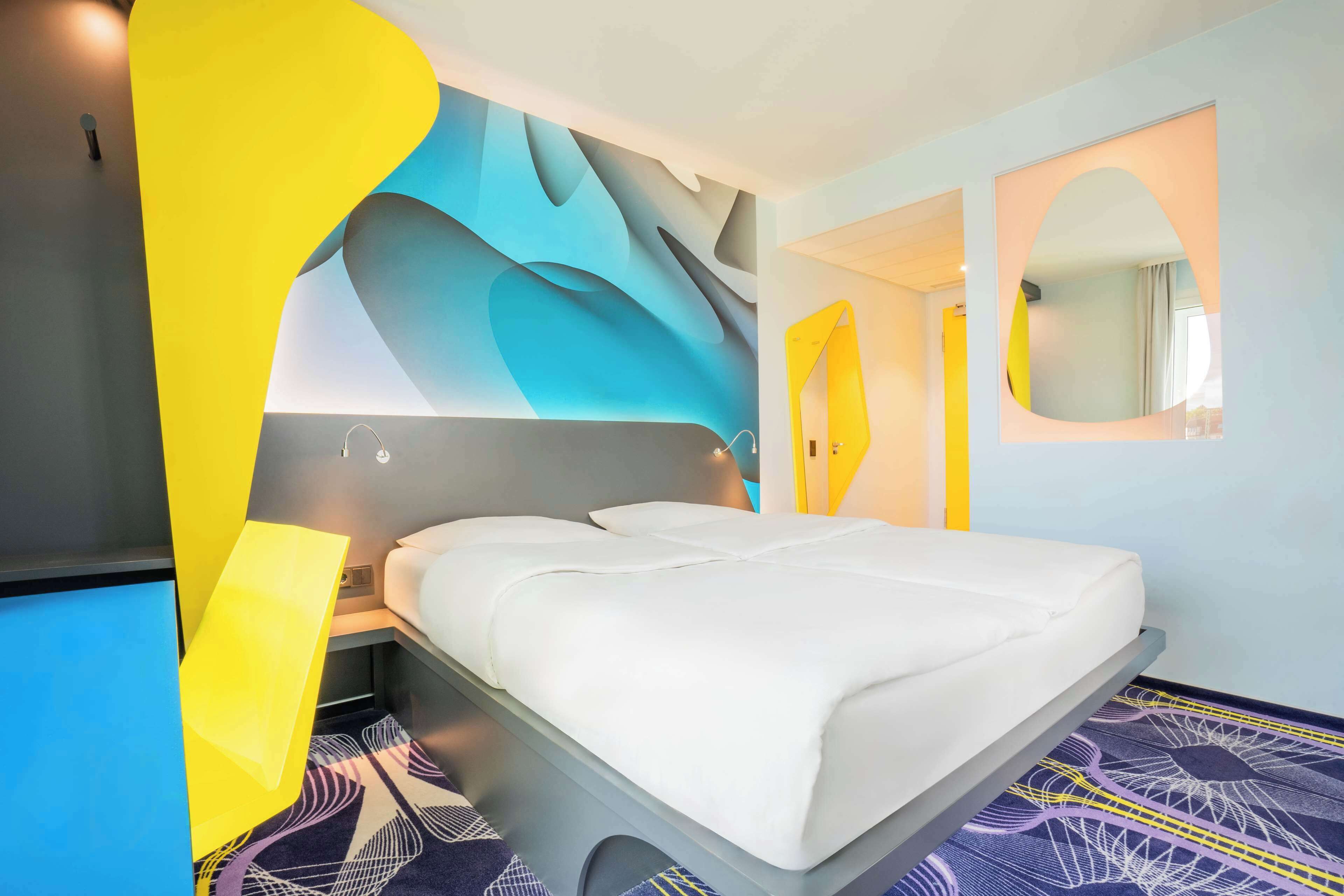 Ein modernes Hotelzimmer mit einem großen Bett, einem Nachttisch und einem an der Wand befestigten Spiegel.