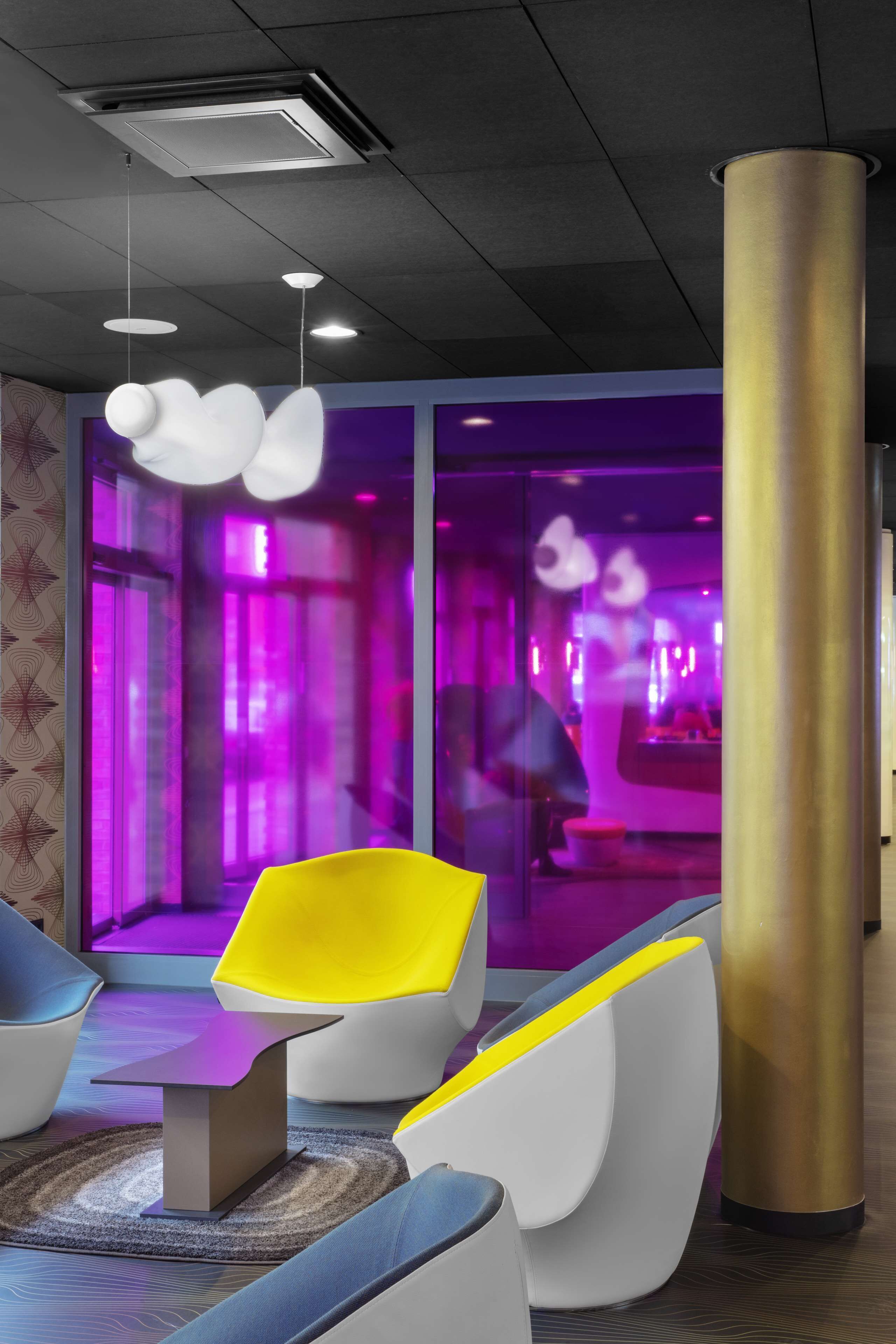 Eine moderne Lobby mit einzigartiger Sitzmöbeln, einer großen Säule und einer Glastrennwand mit violetter Beleuchtung.