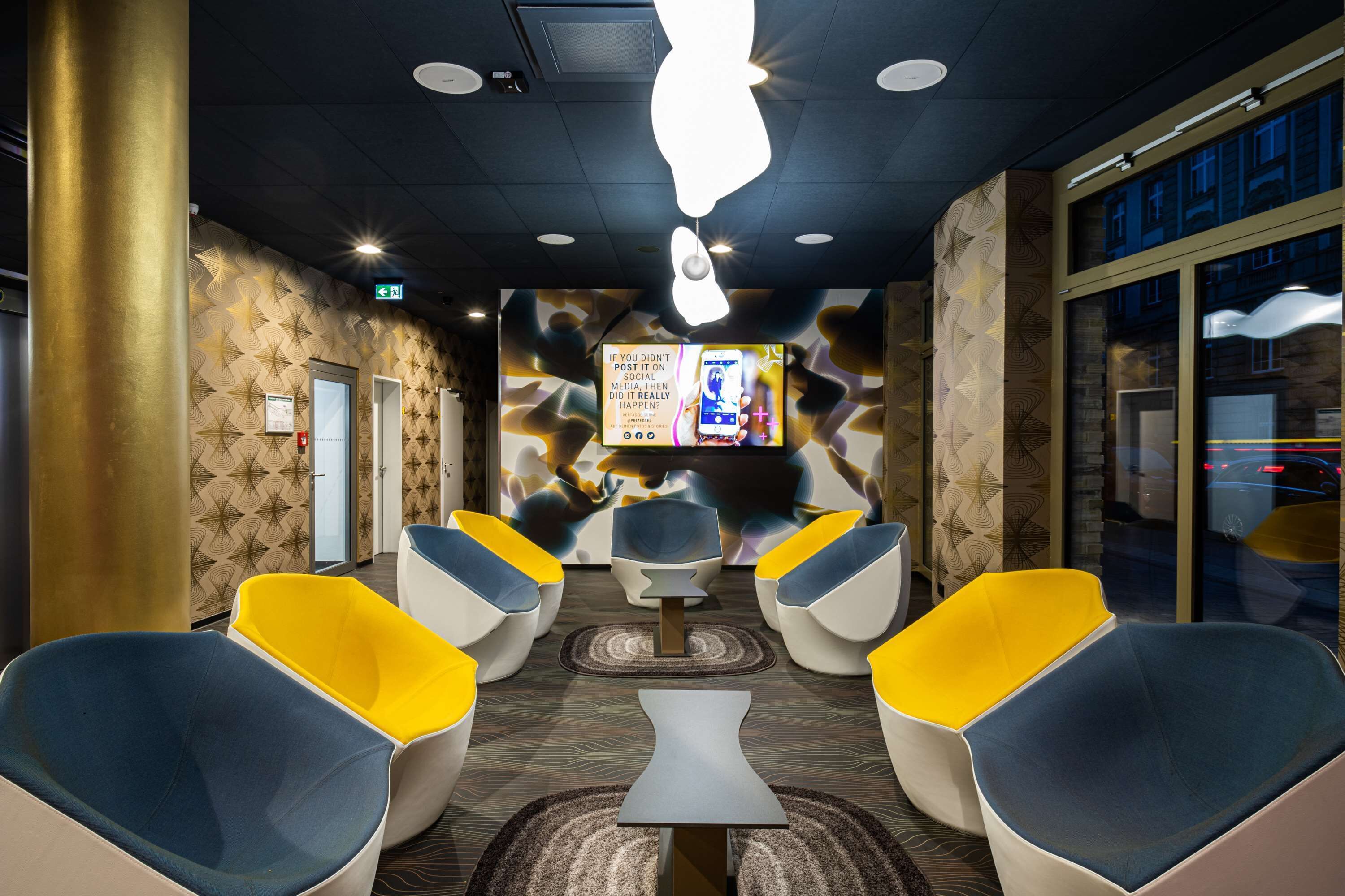 A modern lounge area with unique patterned walls, a central table, and vibrant yellow and blue chairs.