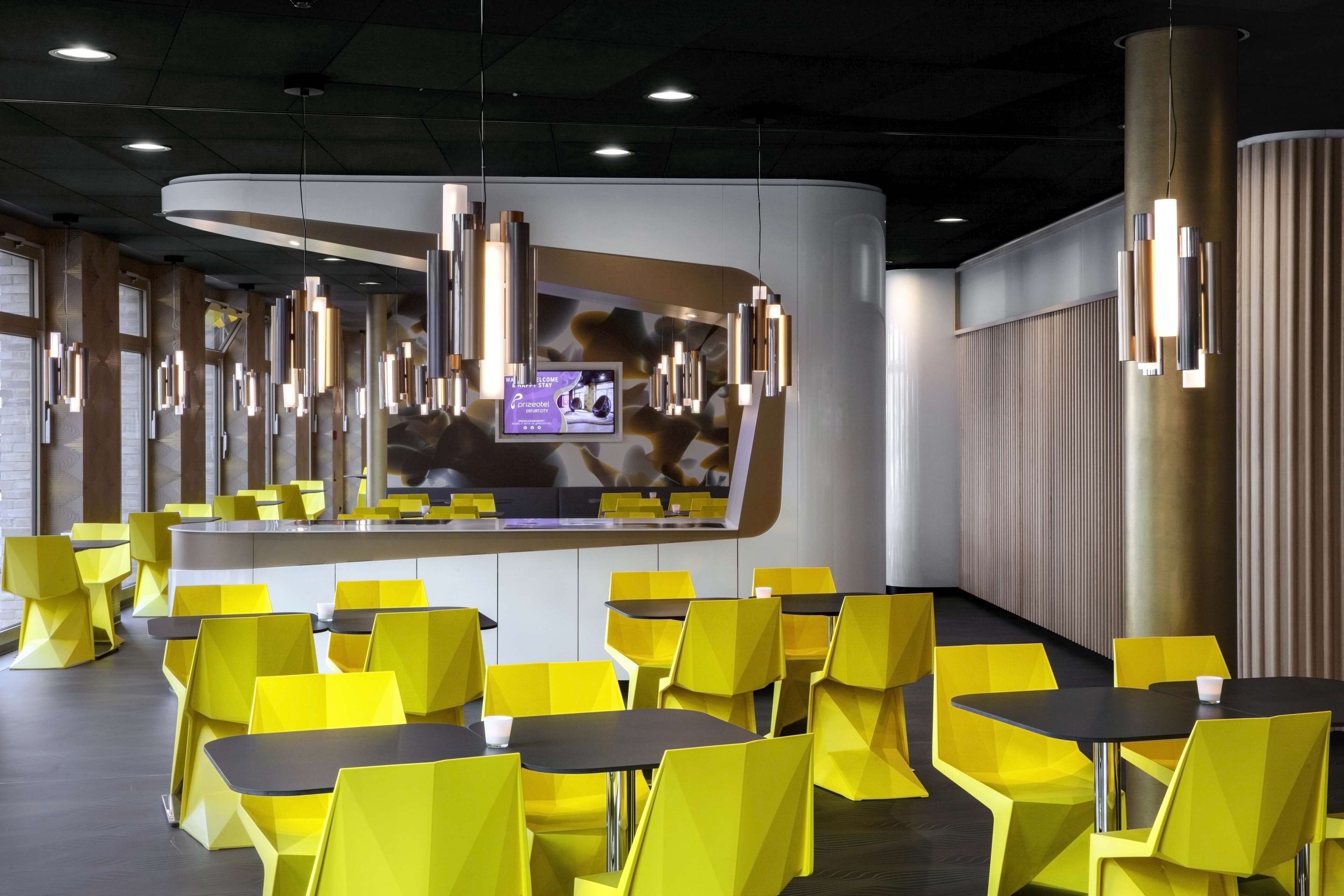 Un interior de restaurante moderno con sillas y mesas amarillas, una barra curva e iluminación colgante.